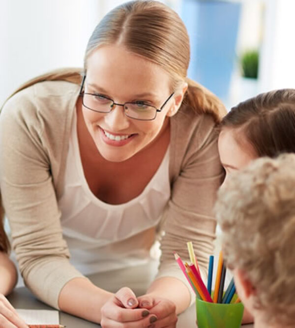 A smiling teacher leaning over a table of small children